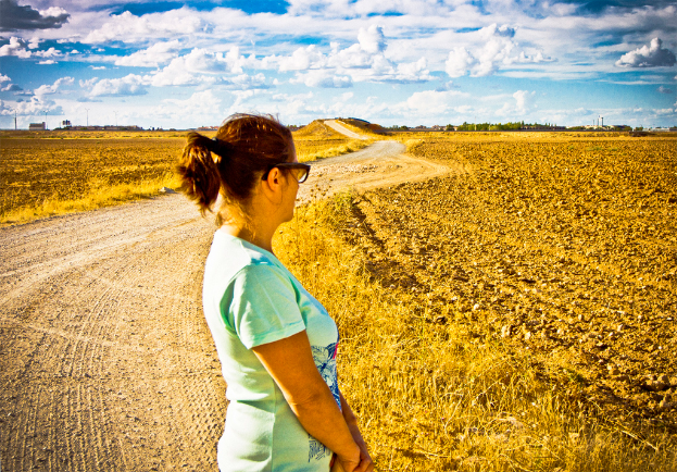 Eine Frau steht auf einem schlammigen Weg, flankiert von Landwirtschaftsland und Bäumen.