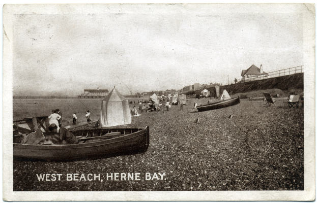 Schwarz-weiß-Foto von Menschen am Weststrand in Herne Bay mit Booten im Vordergrund, H├Ąusern und einem Zaun im Hintergrund und Text am unteren Rand.