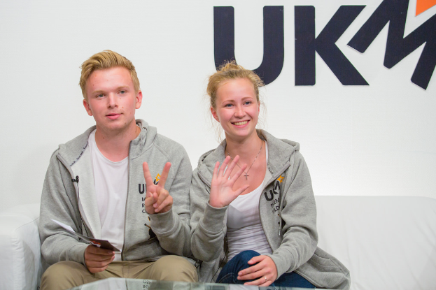 Ein Paar mit passenden Jacken sitzt auf einem Sofa mit "UKM" im Hintergrund.