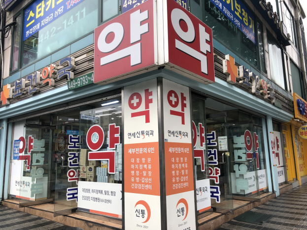 Außenansicht eines modernen Glaswand-Pharmagebäudes in Seoul, Südkorea, mit Text, der darauf hinweist, dass es das erste Pharmageschäft in der Stadt ist.