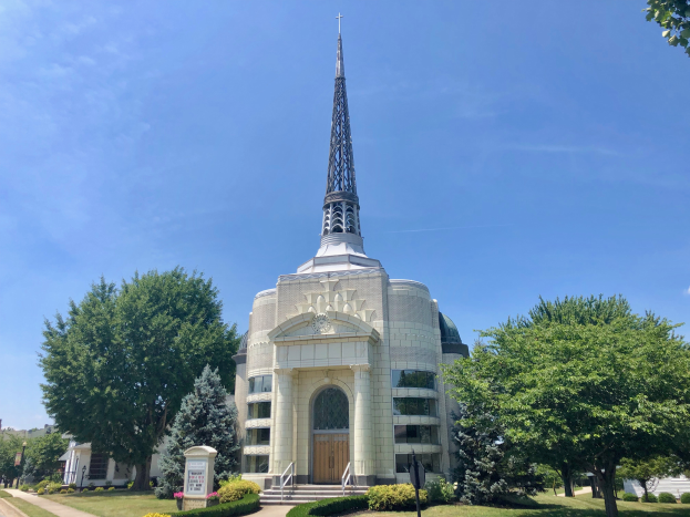 Die St. Mary's Episcopal Church, ein großes weißes Gebäude mit einem Turm, umgeben von Bäumen, Pflanzen und Gras, mit einem bewölkten Himmel im Hintergrund.