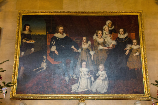 Ein gerahmtes Bild einer Familie in einem Raum mit einem Weihnachtsbaum, flankiert von zwei Fotorahmen, mit dekorativen Gegenständen darunter.