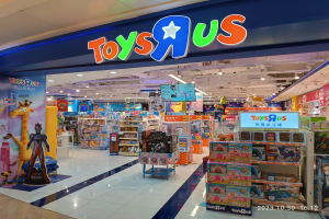 Ein Toys R Us Geschäft in einem Einkaufszentrum, mit Regalen voller Spielzeug, einem Namensschild mit Text, Deckenbeleuchtung und einem Wasserzeichen in der rechten unteren Ecke.