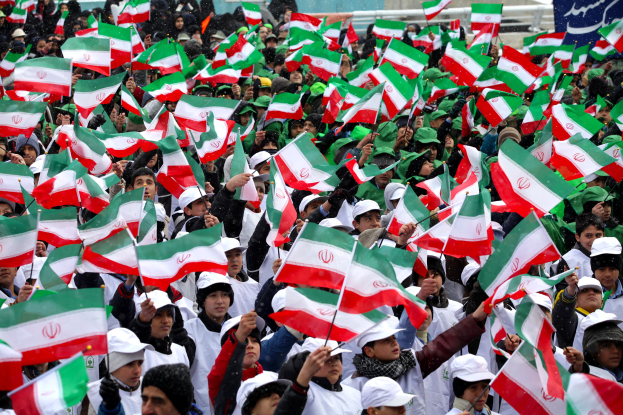Eine große Menschenmenge mit iranischen Flaggen vor einem Gebäude, mit einer Fahne auf der rechten Seite und ein paar Menschen im Hintergrund.