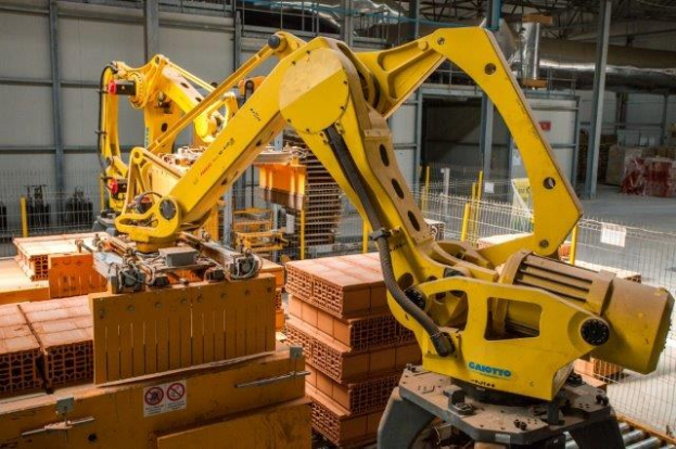 Großes Industriegelände mit gestapelten Kisten, Kränen, Zaun, Strommasten und einer fernen Begrenzungsmauer.