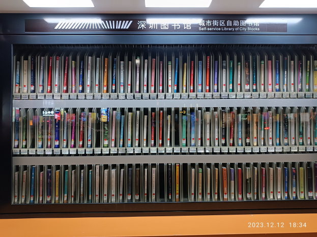 Eine gut beleuchtete Bibliothek mit hohen Bücherregalen voller Bücher, mit einer Tafel mit Text und einem Wasserzeichen unten, ähnlich einer Selbstbedienungsbibliothek in städtischen Straßenzügen.