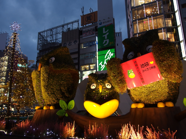 Vögel in der Mitte, Pflanzen unten, ein Weihnachtsbaum links, Gebäude im Hintergrund und Banner mit Text.