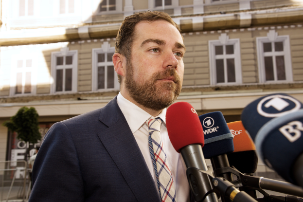 Ein Mann im Anzug und Krawatte steht vor Mikrofonen und spricht zur Presse vor einem Gebäude, nachdem er zu drei Jahren Haft verurteilt wurde.