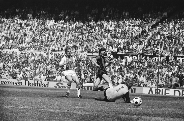 Schwarzes Foto von Männern, die auf einem Feld Fussball spielen, mit Zuschauern im Hintergrund und einer Banner mit der Aufschrift "Bundesliga 1978-79 Ajax 1-1 Hannover 96".