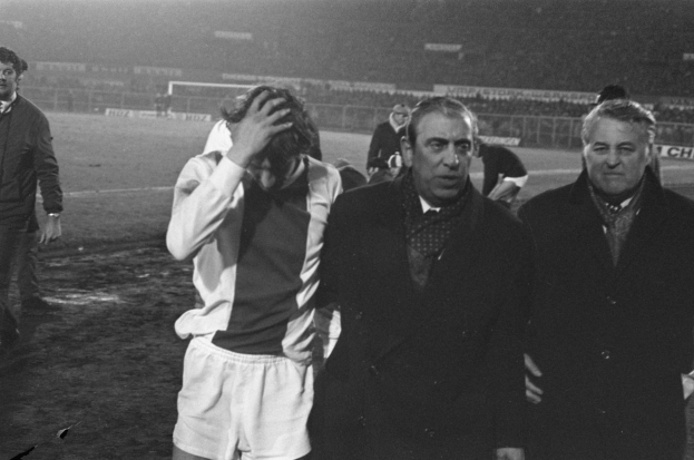 Eine Gruppe von bedrückten Männern in schwarz-weißer Kleidung steht zusammen auf einem Fußballfeld, im Hintergrund ist ein Stadion zu sehen, wahrscheinlich nach einem gewonnenen Spiel.