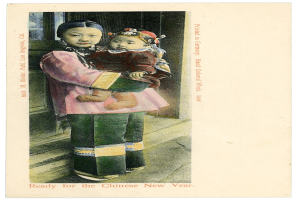 Eine alte Postkarte mit einer Frau, die ein Baby im Arm hält und beide fröhlich in die Kamera schauen.