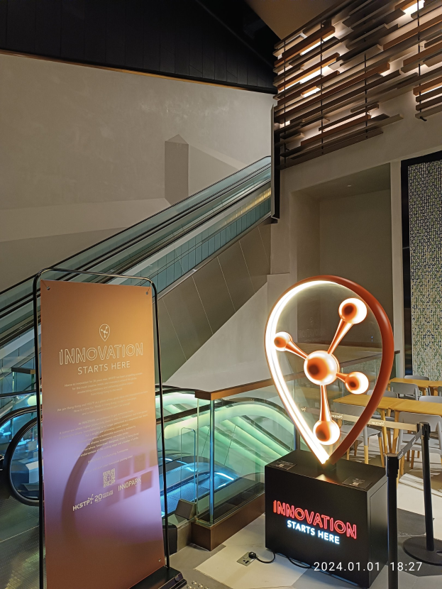 Großes Schild in einem Gebäude mit einer Treppe im Hintergrund, flankiert von Tischen und Stühlen auf der rechten Seite und einer Tafel mit der Aufschrift "Innovation beginnt hier" auf der linken Seite, was die Teilnahme an der HSTP20 Expo anzeigt.