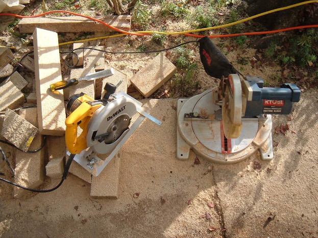 Ein Holzschneidemaschine umgeben von Holzstöcken und Drähten, mit Gras oben und Boden im Hintergrund.