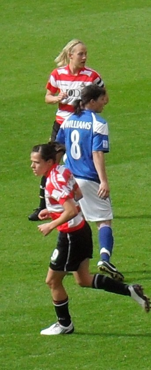 Drei Frauen in Sportuniformen spielen Fussball auf einem grünen Feld.