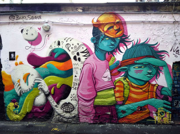 Mural an einem Gebäude mit Graffiti, das eine Straße am Boden, Strommasten und einen klaren blauen Himmel im Hintergrund zeigt.