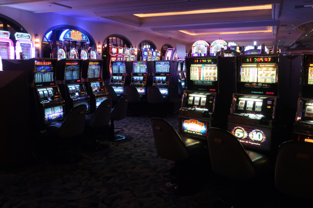 Eine Reihe von Spielautomaten in einem Casino, jeder mit Text und Zahlen, die darauf hinweisen, dass sie zum Verkauf stehen, mit Stühlen auf dem Boden und Lampen an der Decke.