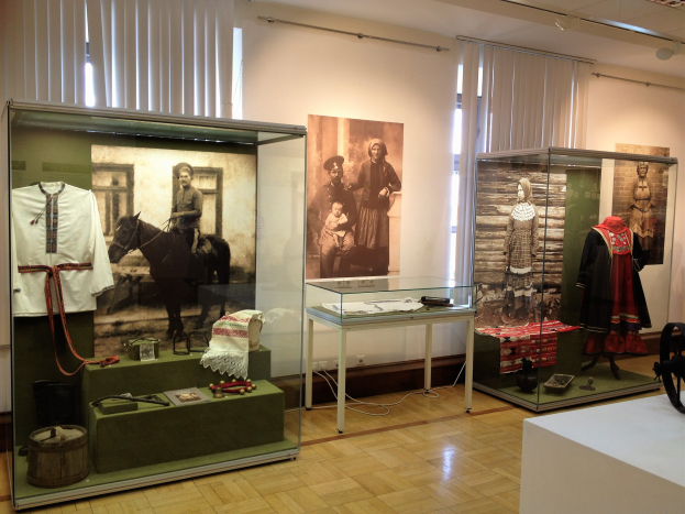 Ein Raum im Polen-Museum in Warschau, Polen, voller Glasboxen mit Kost├╝men tragenden Schaufensterpuppen, einem Tisch mit verschiedenen Gegenst├Ąnden, Fotorahmen an den W├Ąnden, Fenstern mit Vorh├Ąngen und Deckenleuchten.
