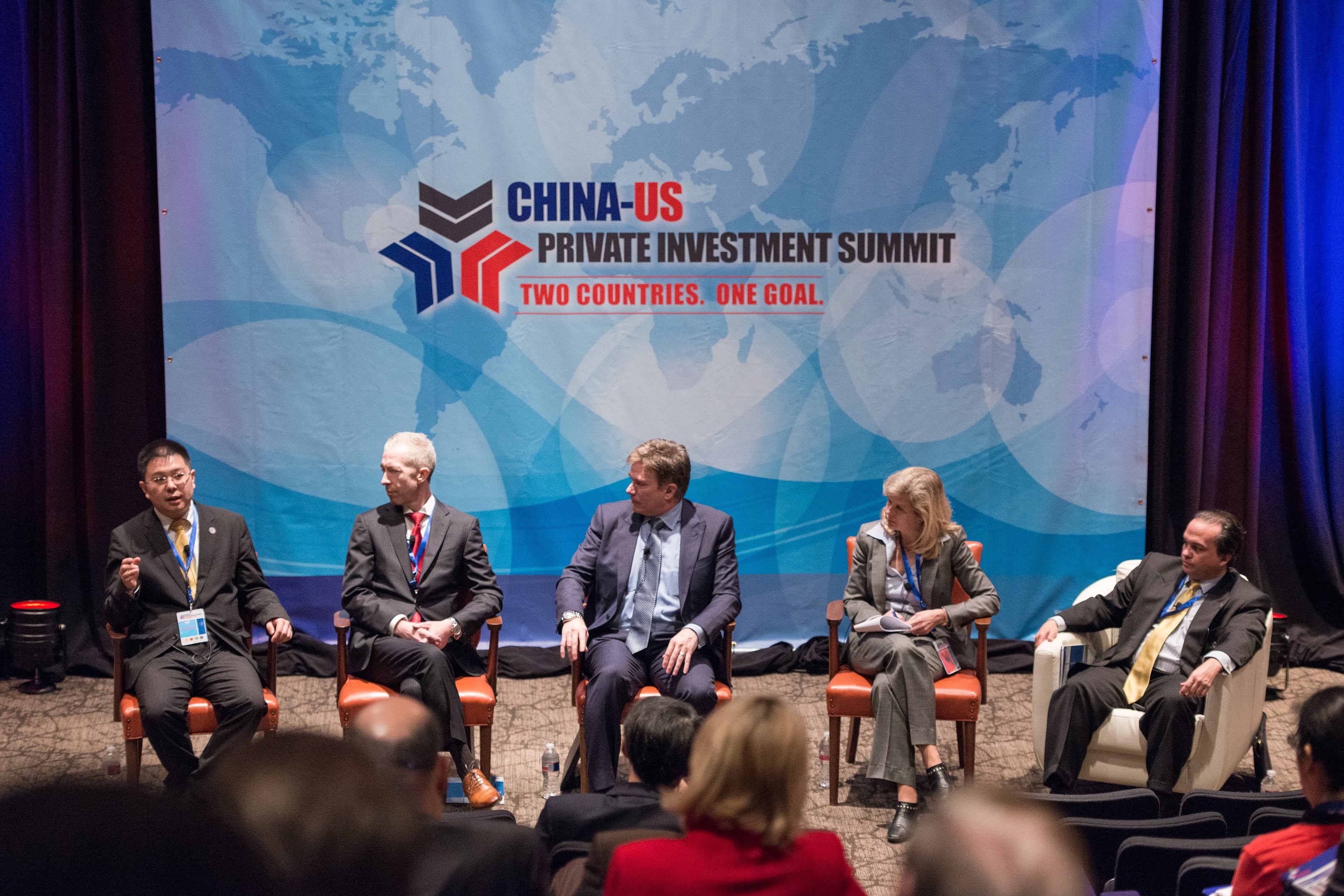 Eine Gruppe von Menschen, die auf Stühlen sitzen und einem Bildschirm mit Text und einer Karte gegenübersitzen, mit Vorhängen im Hintergrund, was auf einen China-US-Privatinvestment-Gipfel hinweist.
