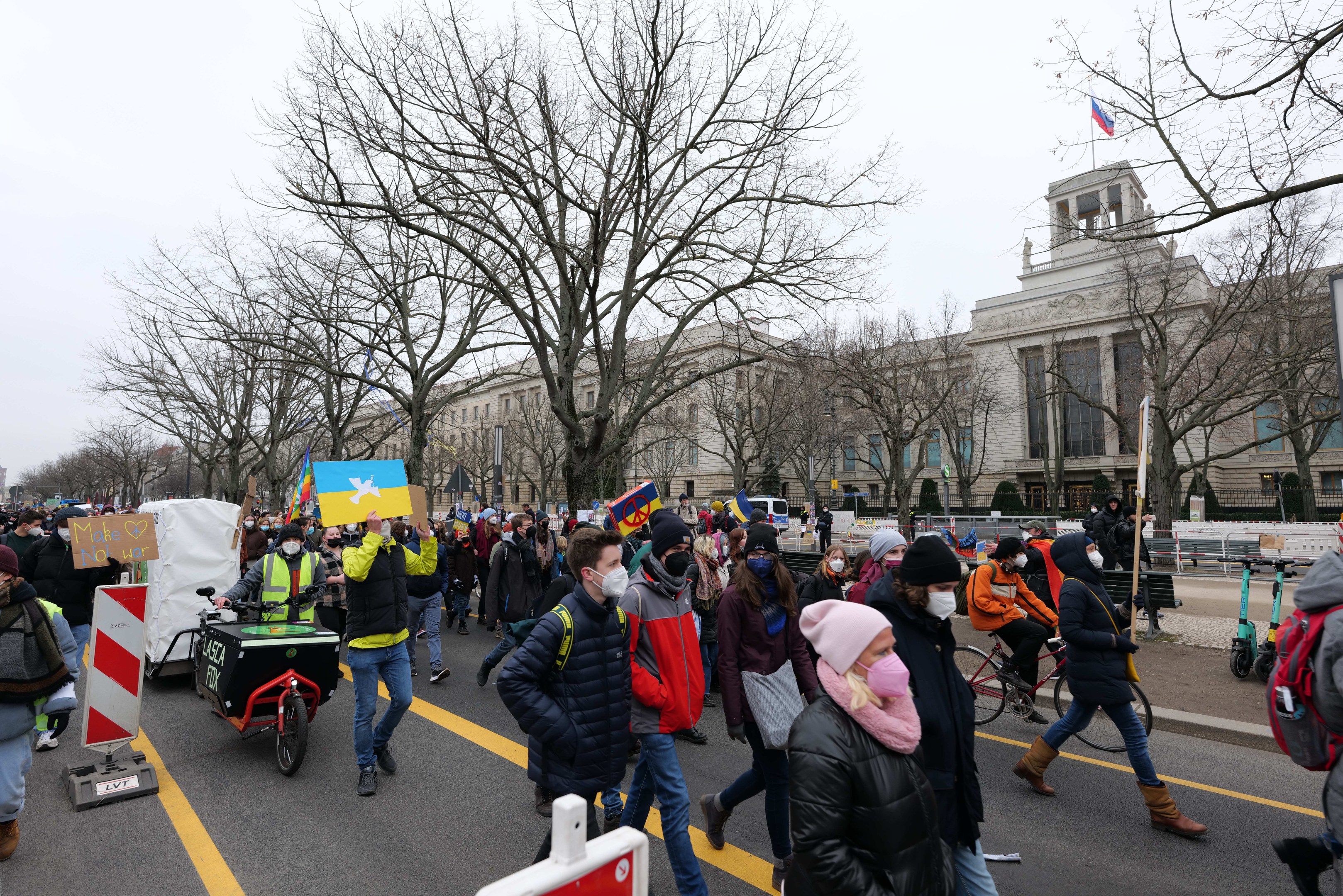 Eine große Gruppe von Menschen marschiert auf einer Straße in Washington, D.C. und hält Schilder und Banner, während einige Fahrräder fahren, unter einem klaren blauen Himmel.