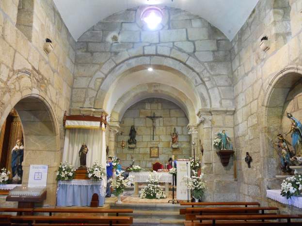 Innenansicht einer Kirche mit zahlreichen Skulpturen und Topfpflanzen um leere Holzliegen.