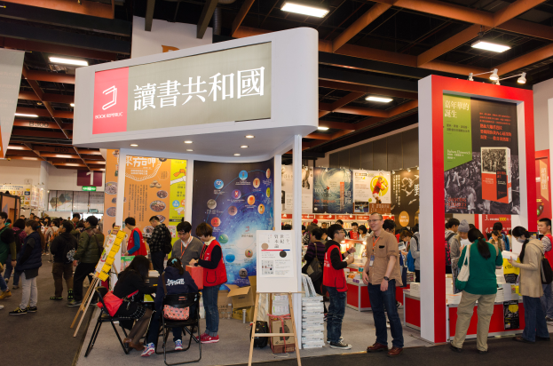Eine große Gruppe von Menschen an einem Messestand mit der Aufschrift "Book Republic Hong Kong Book Fair", Banner und Deckenbeleuchtung.