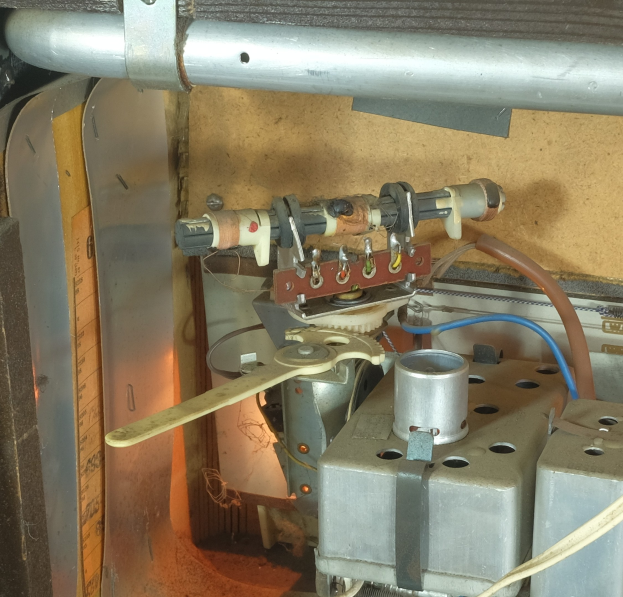 Nahaufnahme eines Gasofens mit einem angebrachten Schlauch, umgeben von Metallobjekten, Rohren und verstreuten Werkzeugen und Materialien, was darauf hinweist, dass er repariert wird.